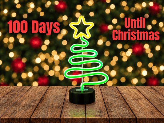 Glowing green neon Christmas tree light on a wooden table with text reading 100 Days Until Christmas