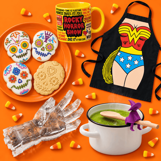 Halloween gifts on an orange background: sugar skull cookies, a Rocky Horror Show mug, a Wonder Woman apron, a clear ice zombie hand, and a witch spoon holder on a pot.