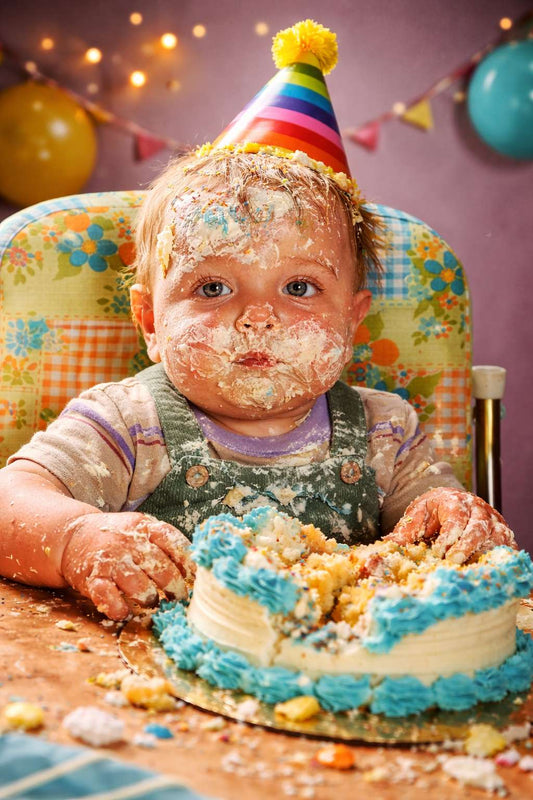 Toddler covered in birthday cake with frosting on face and hair at a retro-style party, illustrating 2025 birthday trends focused on cake-centred celebrations.
