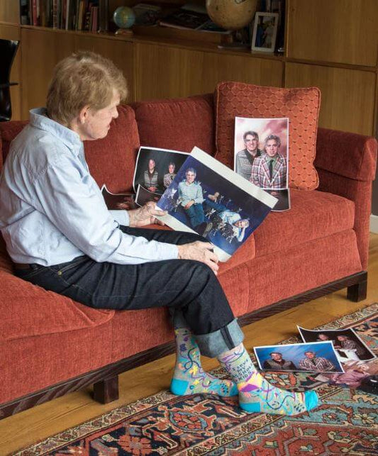 Elderly person sitting on a couch, wearing colorful socks, looking at family photographs.