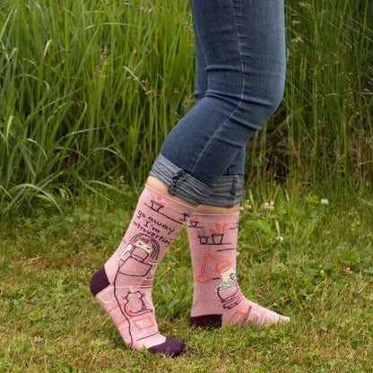 Go Away I’m Introverting funny novelty socks by Danna Bananas, shown being worn outdoors with rolled jeans, featuring a cozy pink and purple design with a cat and tea theme.