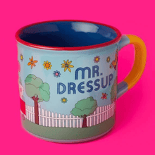 Mr. Dressup ceramic mug with colourful flowers, trees and a white picket fence, blue interior, red rim and yellow handle.