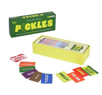 A yellow box labeled "Pickles The Quick Action Party Game" from Danna Bananas contains a card game with various colored cards spread around it. Each card features different words, such as "SWEET!" and "SO SO." The box has a green cover and the game pieces are arranged in an organized layout.