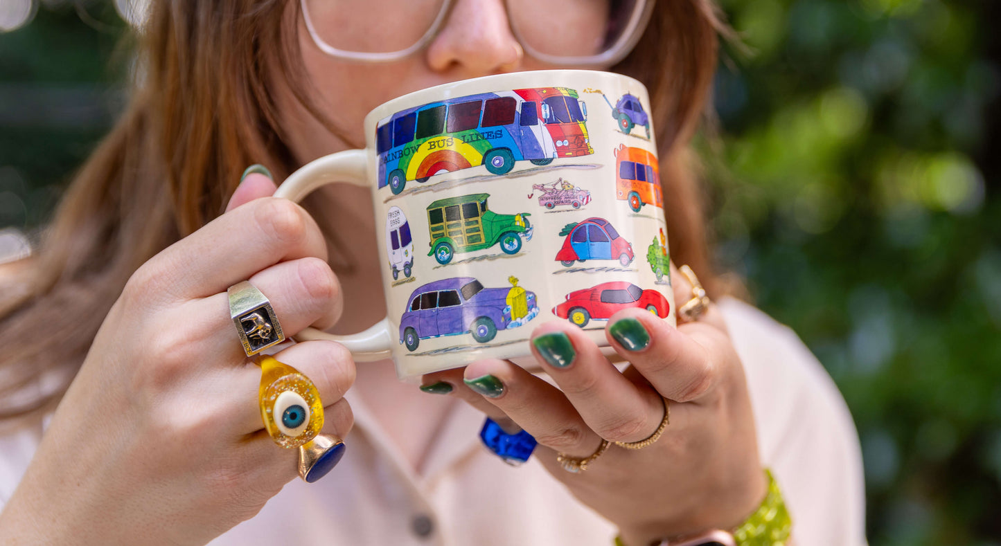 Woman drinking a hot beverage from the Richard Scarry Cars and Trucks Mug, showing the colourful Busytown vehicles on the cold mug