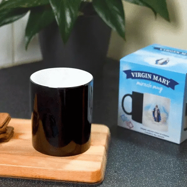 a black Virgin Mary Miracle mug on a wooden tray next to a box of cookies. with the Virgin Mary Miracle Mug behind it