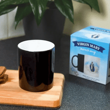 a black Virgin Mary Miracle mug on a wooden tray next to a box of cookies. with the Virgin Mary Miracle Mug behind it
