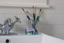 The Joy of Bathing Bob Ross Soap on the back of the sink with a jar of paint brushes