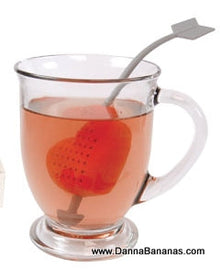 The Tea to My Heart Tea Infuser by Danna Bananas is a glass mug filled with tea featuring a unique, heart-shaped infuser. The handle is shaped like an arrow, making this charming accessory the perfect Mother's Day gift for any tea enthusiast.