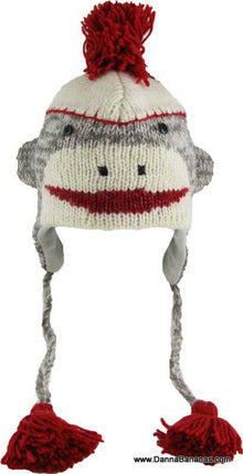 Introducing the Danna Bananas Sock Monkey Pilot Hat - Grey Kids, crafted from premium New Zealand wool. This charming kid-sized hat features a sock monkey design with a white and gray pattern, a red pom-pom on top, a cheeky red mouth, and braided tassels with bright red ends.
