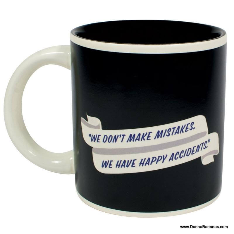 The Bob Ross Self Painting Mug by Danna Bananas showcases a black exterior and white interior, adorned with a white ribbon design and the iconic Bob Ross quote, "We don't make mistakes, we have happy accidents," adding a creative flair to your daily coffee routine.