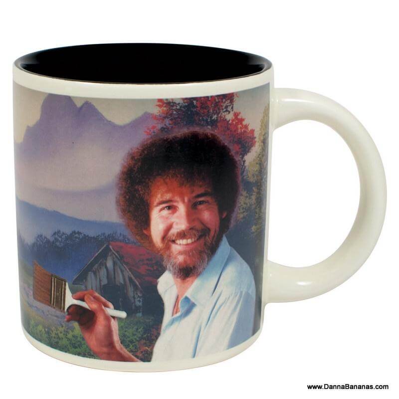 This Bob Ross Self Painting Mug from Danna Bananas features a charming illustration of a curly-haired man, reminiscent of Bob Ross, smiling with a paintbrush in hand. The background presents a tranquil landscape with trees and mountains, making it an ideal addition to any disappearing mugs collection.