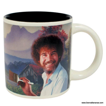 This Bob Ross Self Painting Mug from Danna Bananas features a charming illustration of a curly-haired man, reminiscent of Bob Ross, smiling with a paintbrush in hand. The background presents a tranquil landscape with trees and mountains, making it an ideal addition to any disappearing mugs collection.