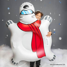 A child smiling and peeking through The Polar Bear Express Big Snow Tube by Danna Bananas, featuring a red scarf and blue sunglasses on the polar bear design. The gray background has snowflake decorations, highlighting the tube's durable construction that ensures endless fun.